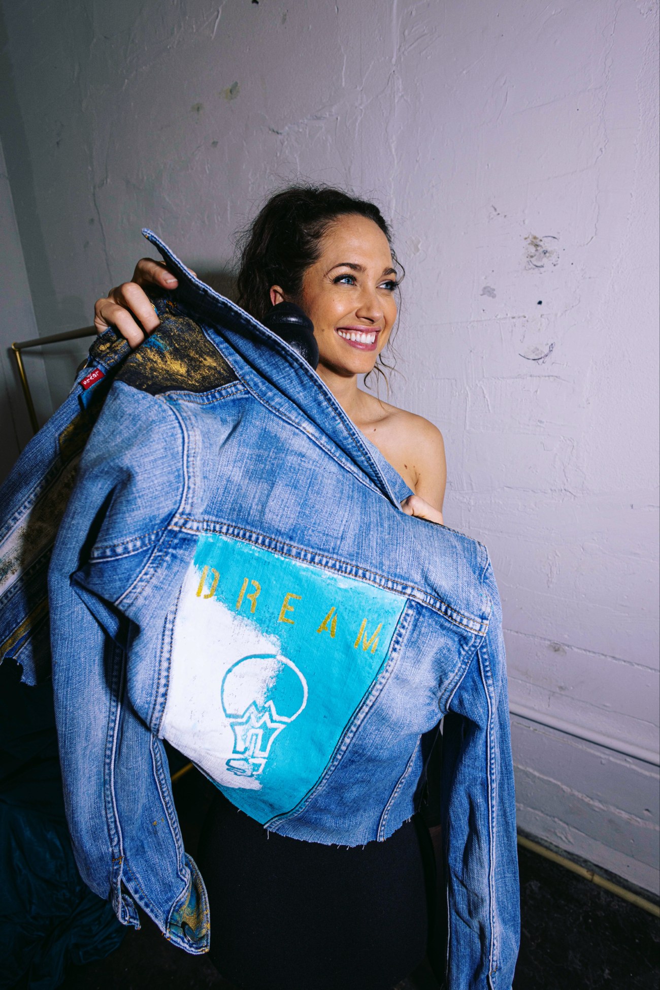 Maiara smiling while holding up her custom painted Dream State denim jacket